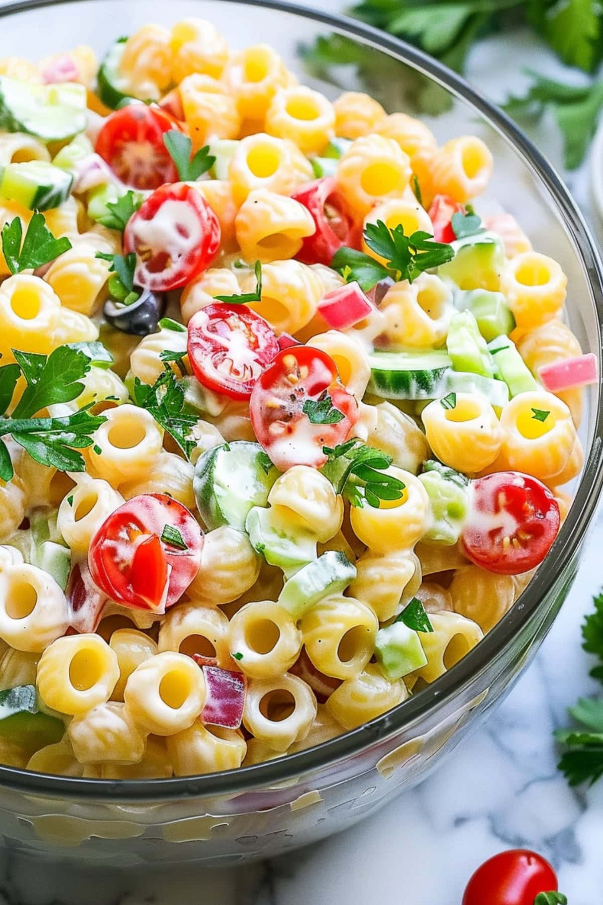 Pasta salad made with ditalini pasta, cherry tomatoes, cucumber, bell pepper, and red onion and creamy dressing tossed in a glass bowl.