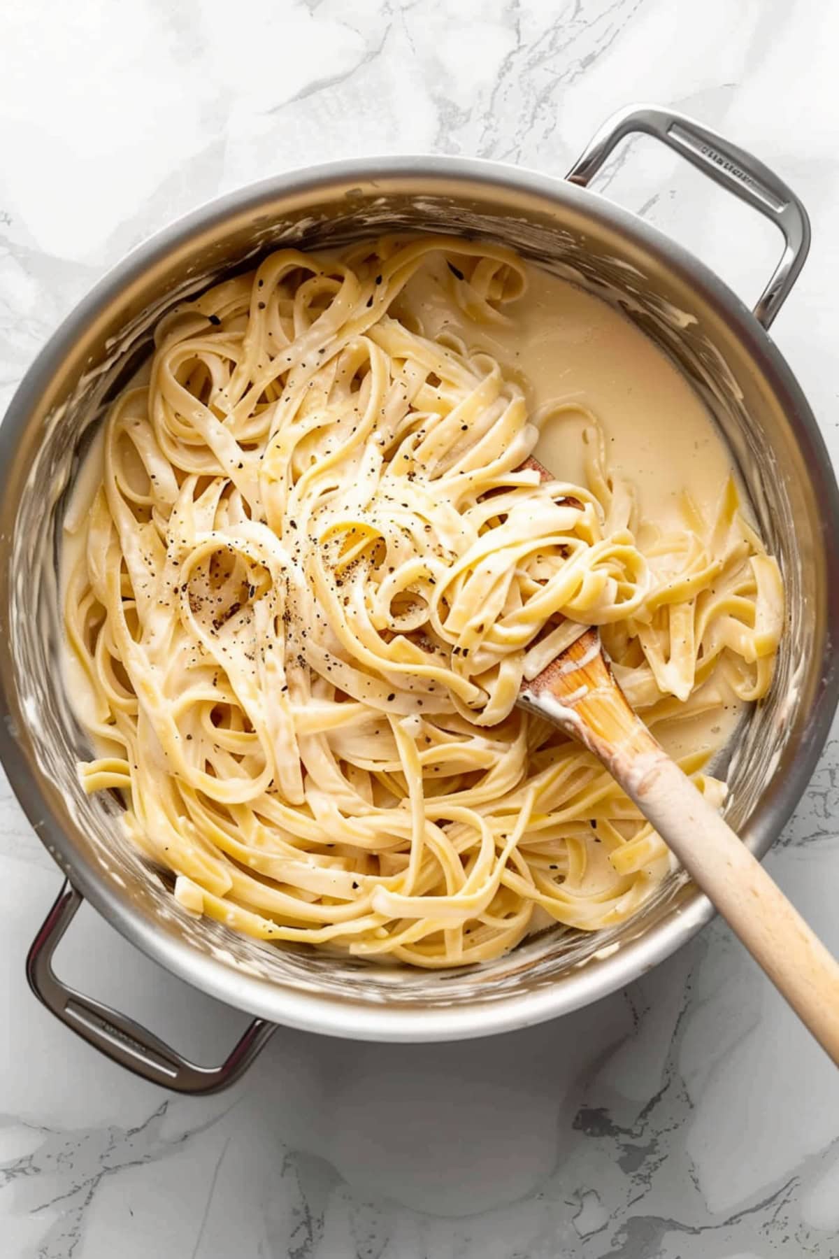 A large pot of creamy fettucine pasta on a white marble countertop.