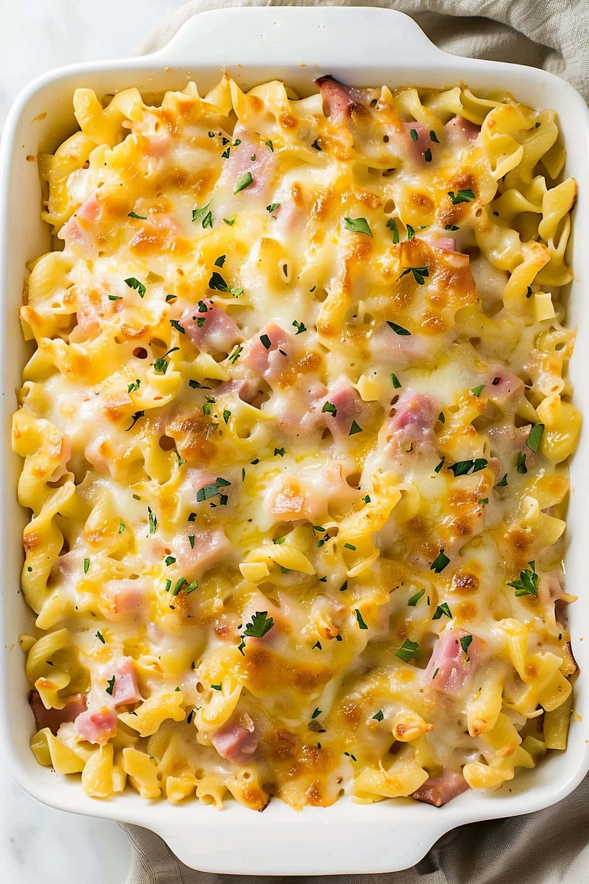 Cheesy homemade ham and noodle casserole in a 9x13 white baking dish.