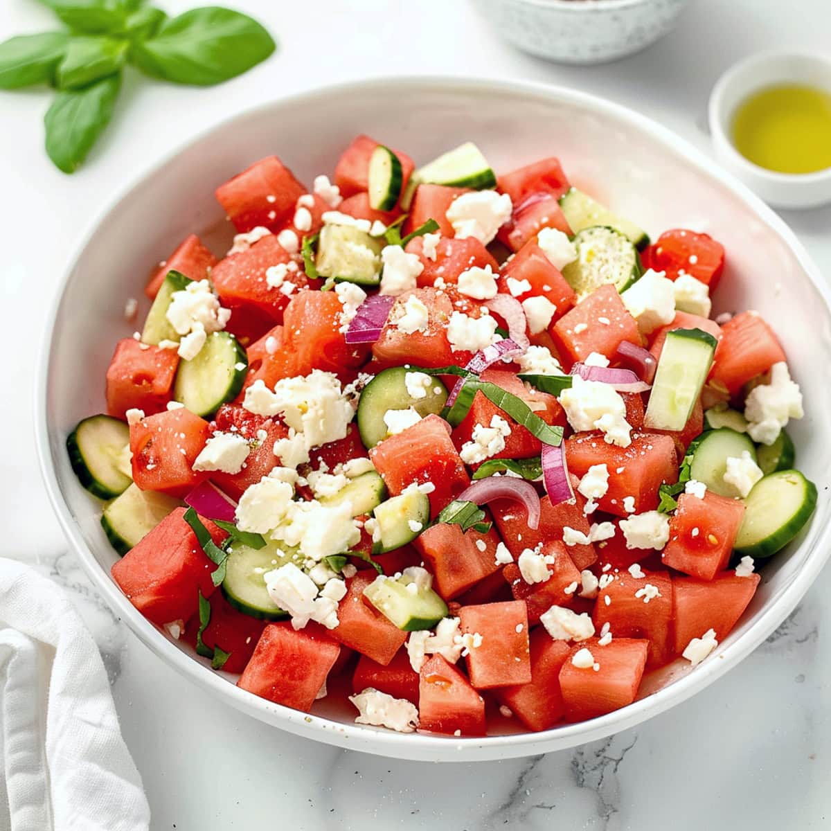 Freshly made watermelon feta salad featuring red onions and cucumbers in a white bowl.