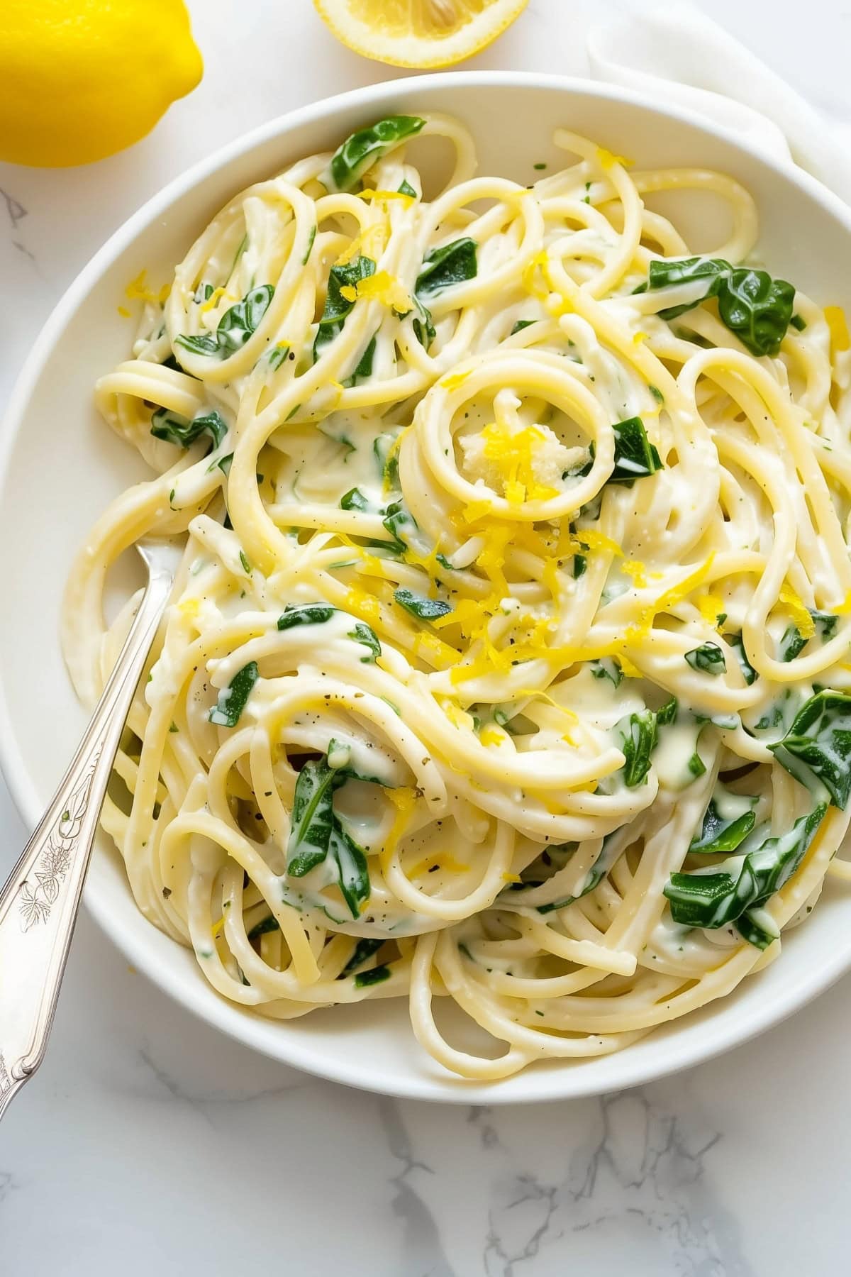Savory lemon ricotta pasta with baby spinach and lemon zest in a white bowl with a fork