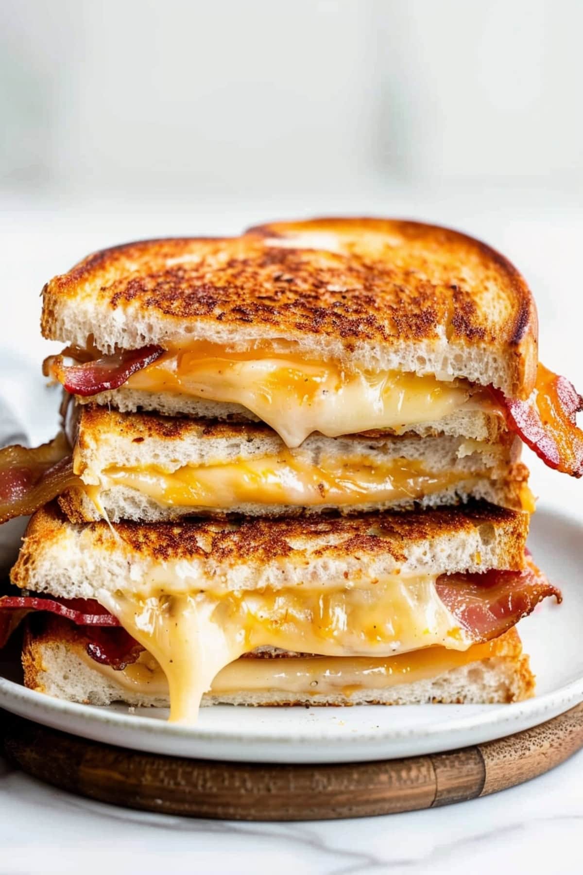Halved bacon grilled cheese sandwiches stacked on a white plate with cheese oozing out