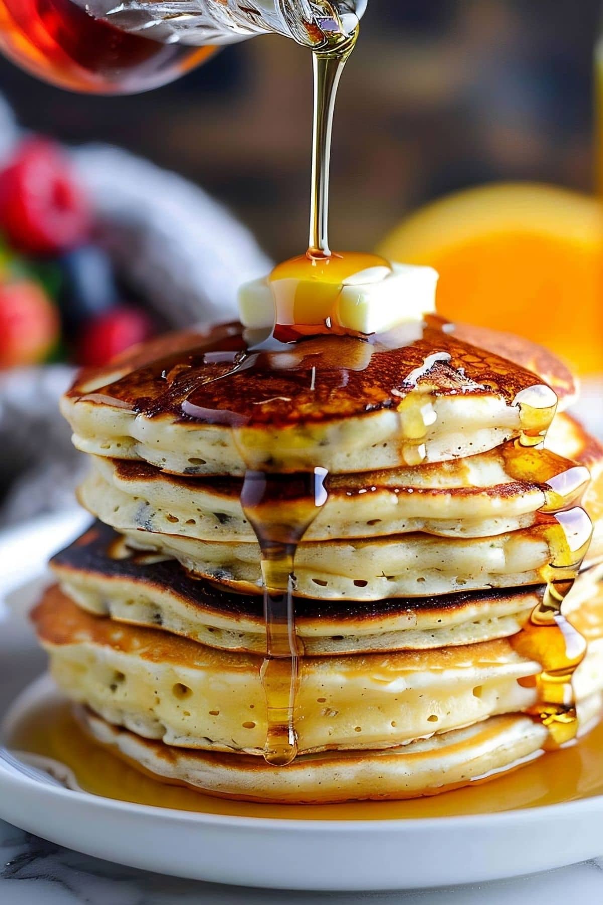 Drizzling Maple Syrup over a Stack of IHOP Pancake Recipe Pancakes with Butter with Fresh Fruit in the Background