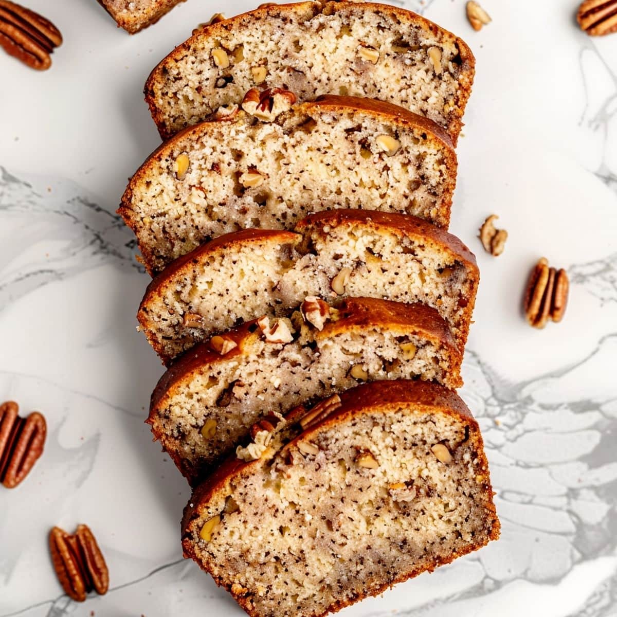 Ina Garten's Banana Bread Slices on a White Marble Table with Pecans