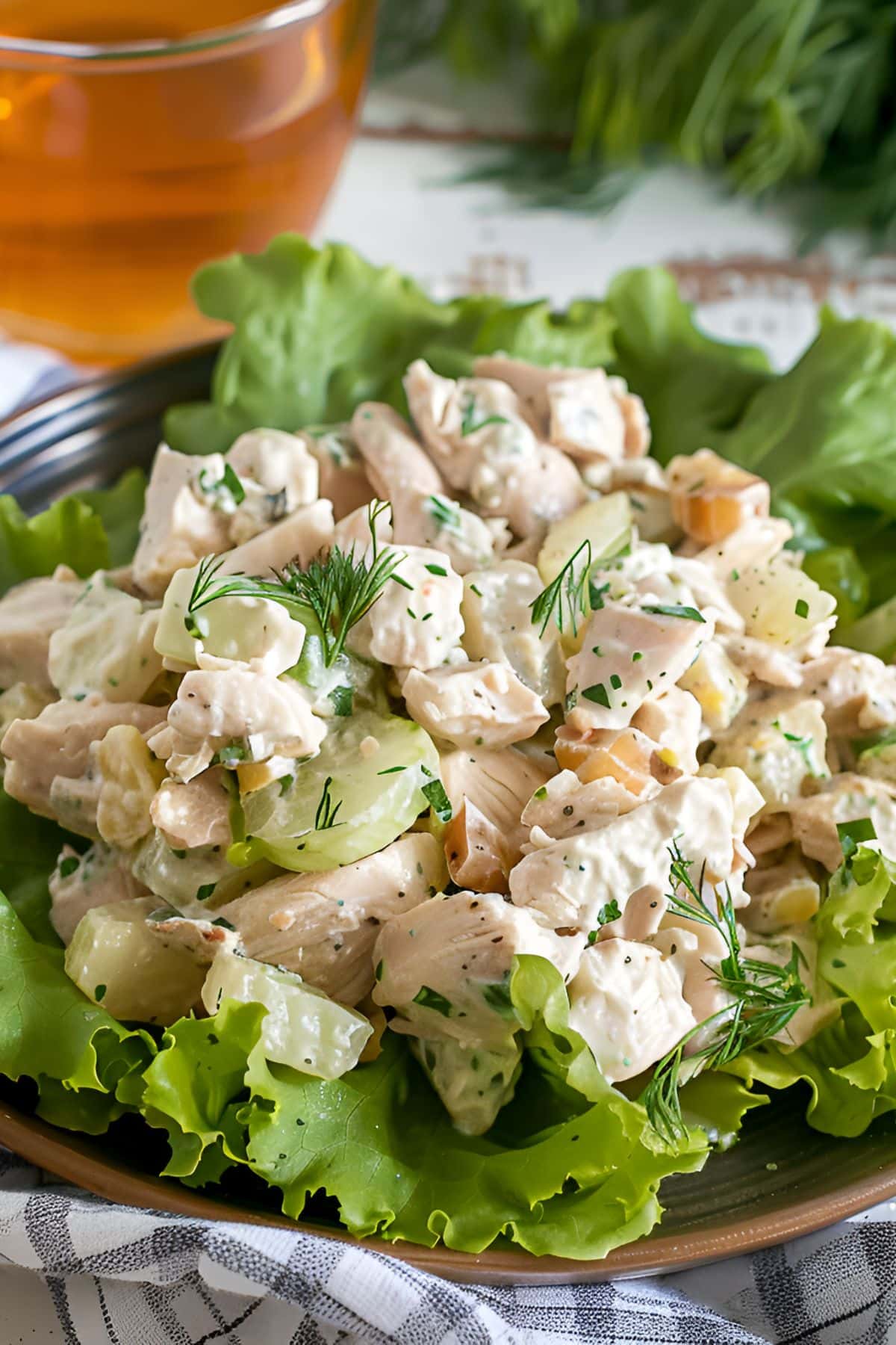 Close Up of Ina Garten's Chicken Salad with Chicken, Dill, Celery, and Mayo on a Bed of Lettuce with a Glass of Tea in the Background