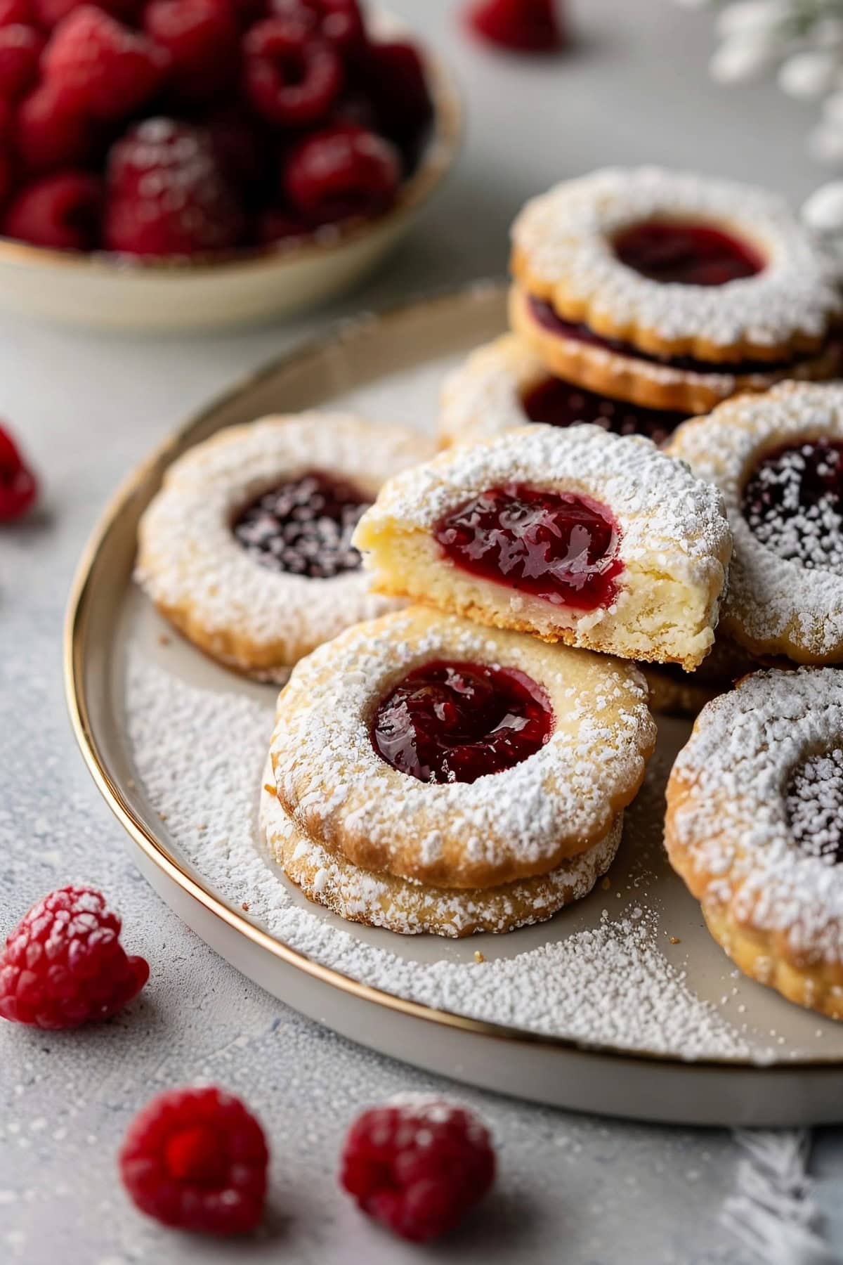 Raspberry Linzer Cookies Dusted with Powdered Sugar on a Plate, One Cookie Cut in Half
