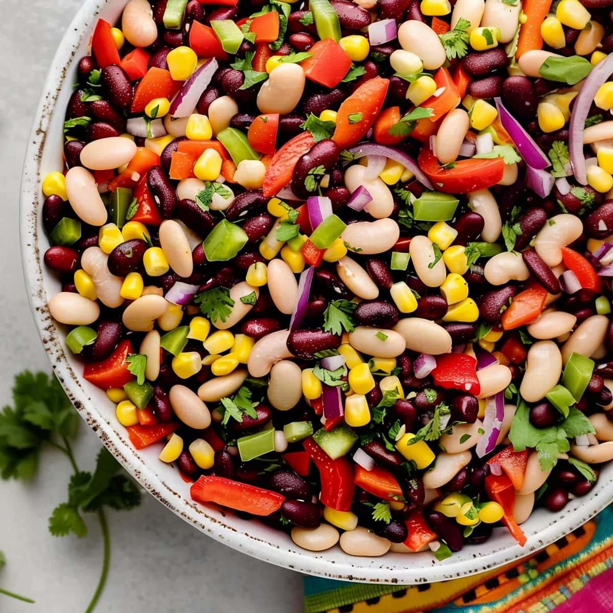 Top View of Mexican Bean Salad in a White Bowl on a White Marble Table with a Colorful Mexican Cloth