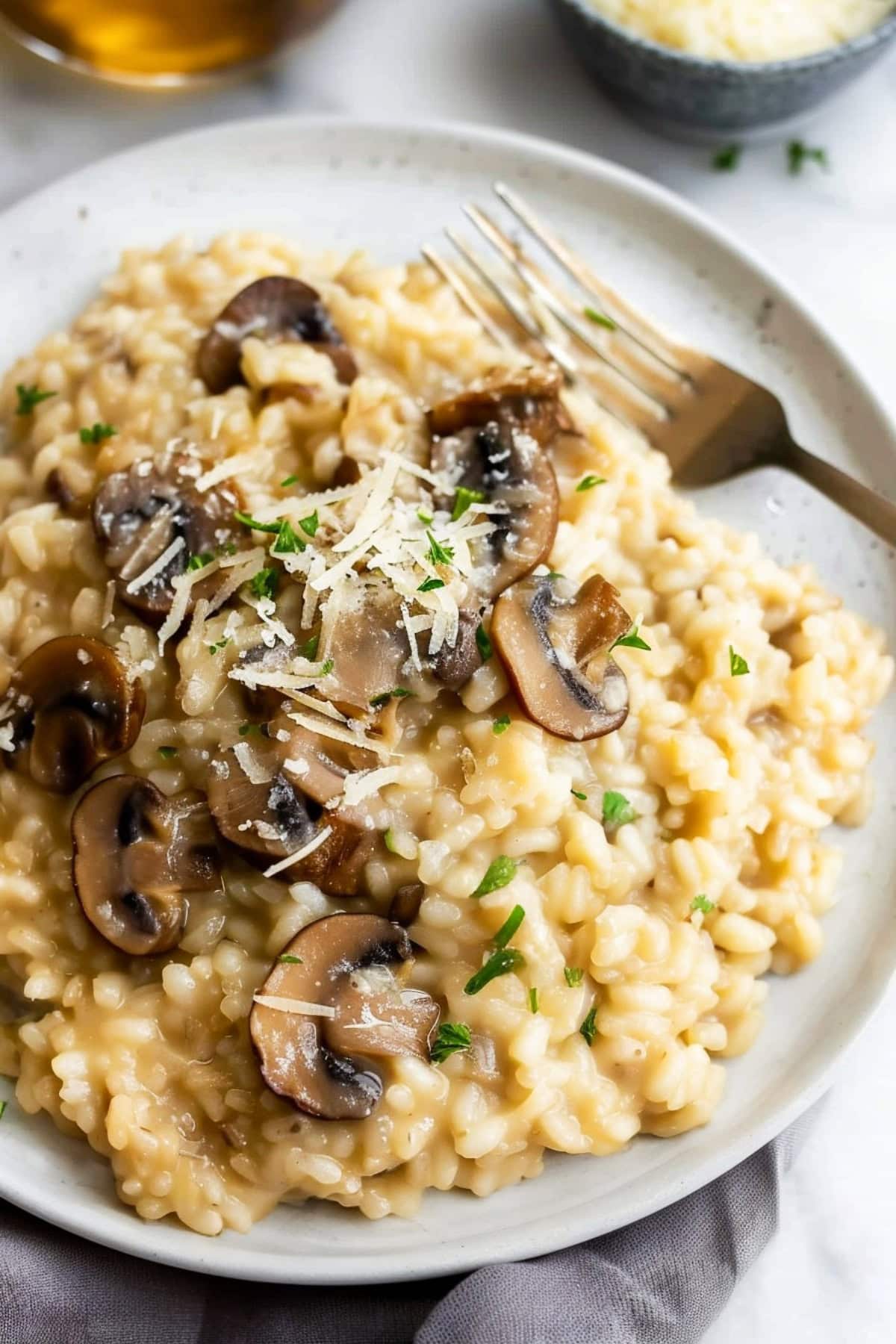 Mushroom risotto served in a white plate, topped with a sprinkle of Parmesan and green parsley.
