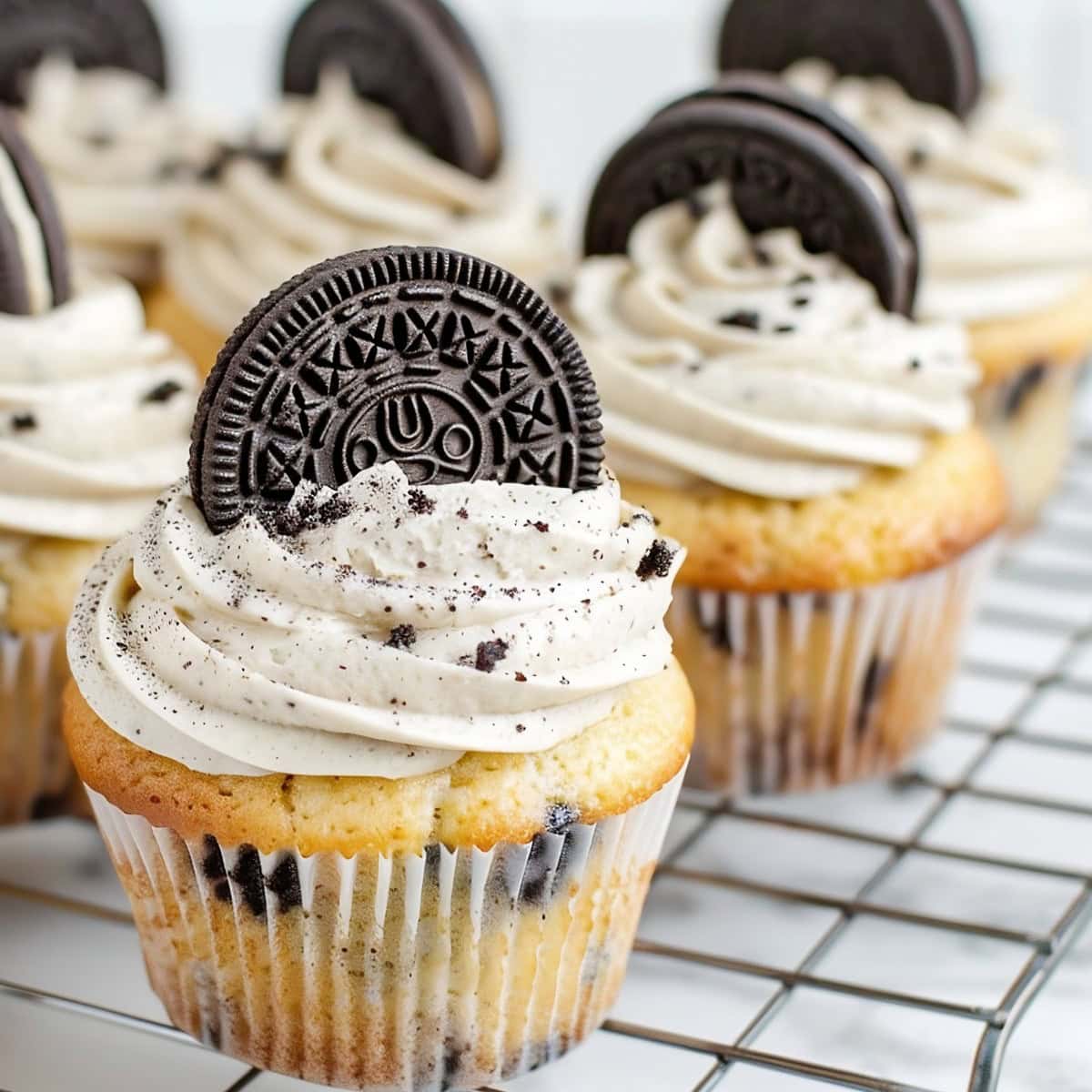 Oreo cupcakes on a cooling rack on a white marble table.