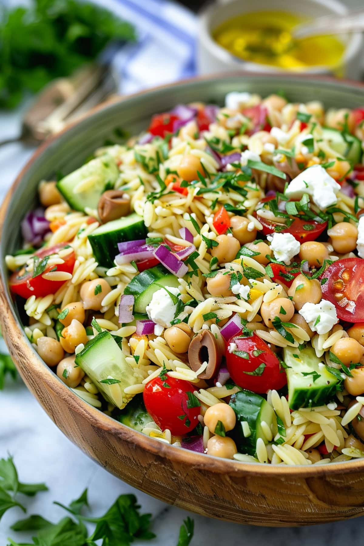 Greek orzo pasta salad made with mix of diced English cucumber, halved cherry tomatoes, drained and rinsed chickpeas, finely chopped red onion, crumbled feta cheese, chopped fresh basil, chopped fresh parsley served in a wooden bowl.