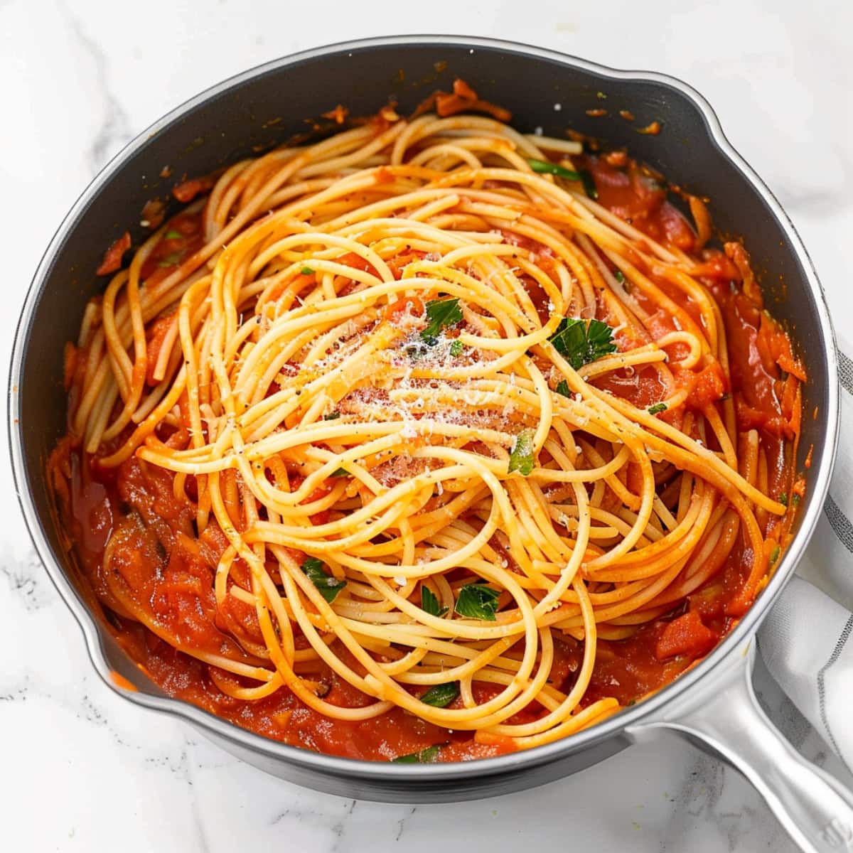 Spaghetti with tomato sauce in a skillet on a white marble table.