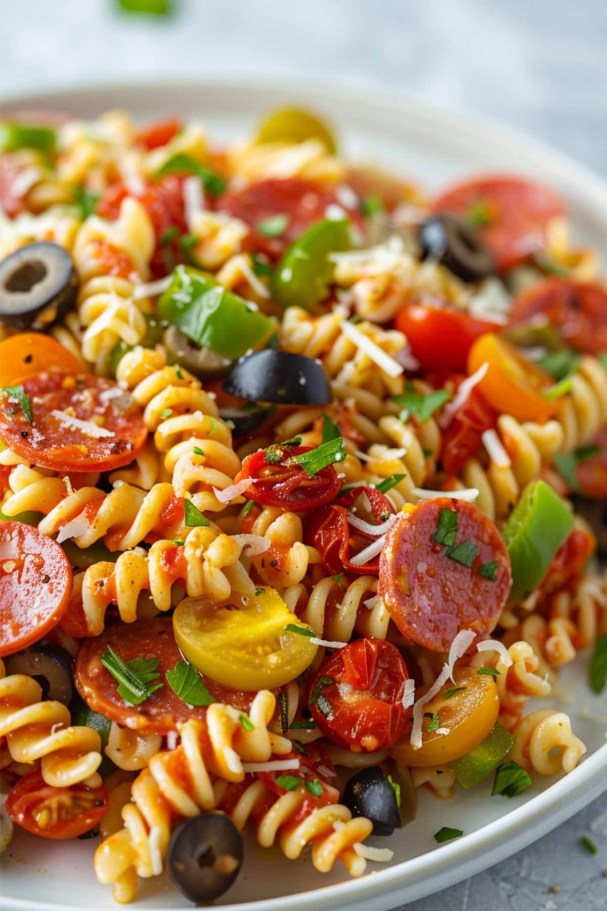 Pepperoni pasta salad with pepperoni, tomatoes, peppers, and olives served on a white plate. 