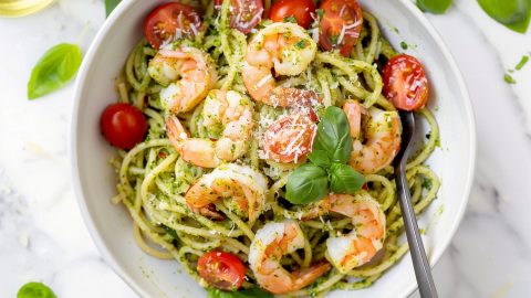 Gourmet pesto shrimp pasta with tomatoes in a white bowl.