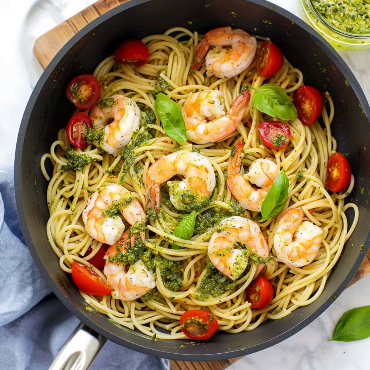 Savory pesto shrimp pasta with cherry tomatoes and basil in a skillet, top view