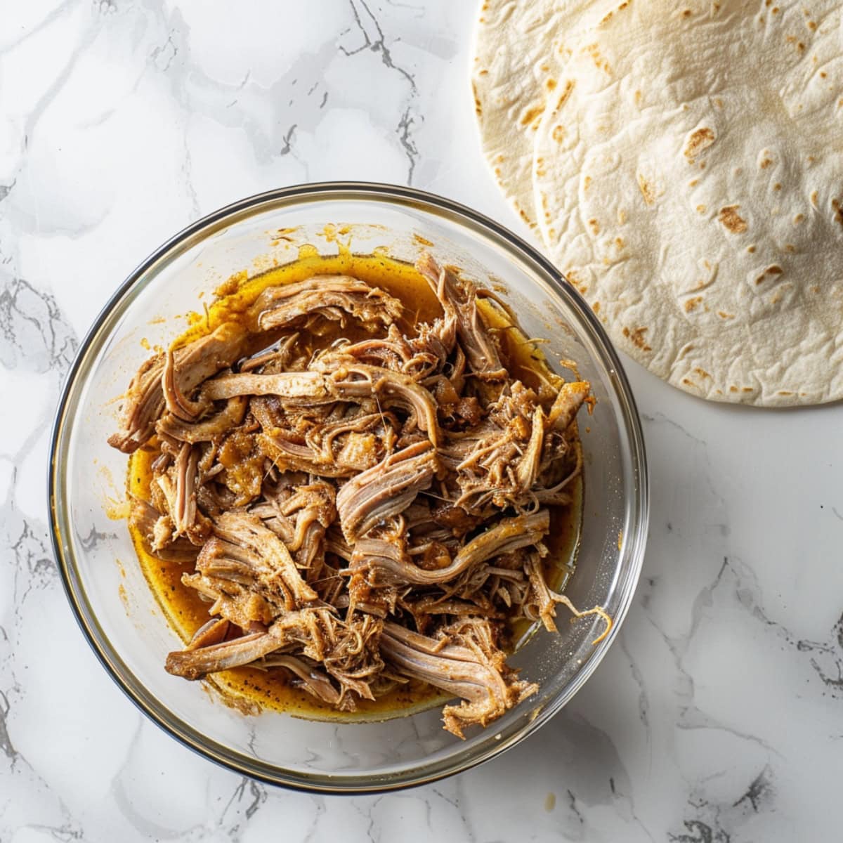 Pulled pork in a glass bowl, corn tortillas on its side. 