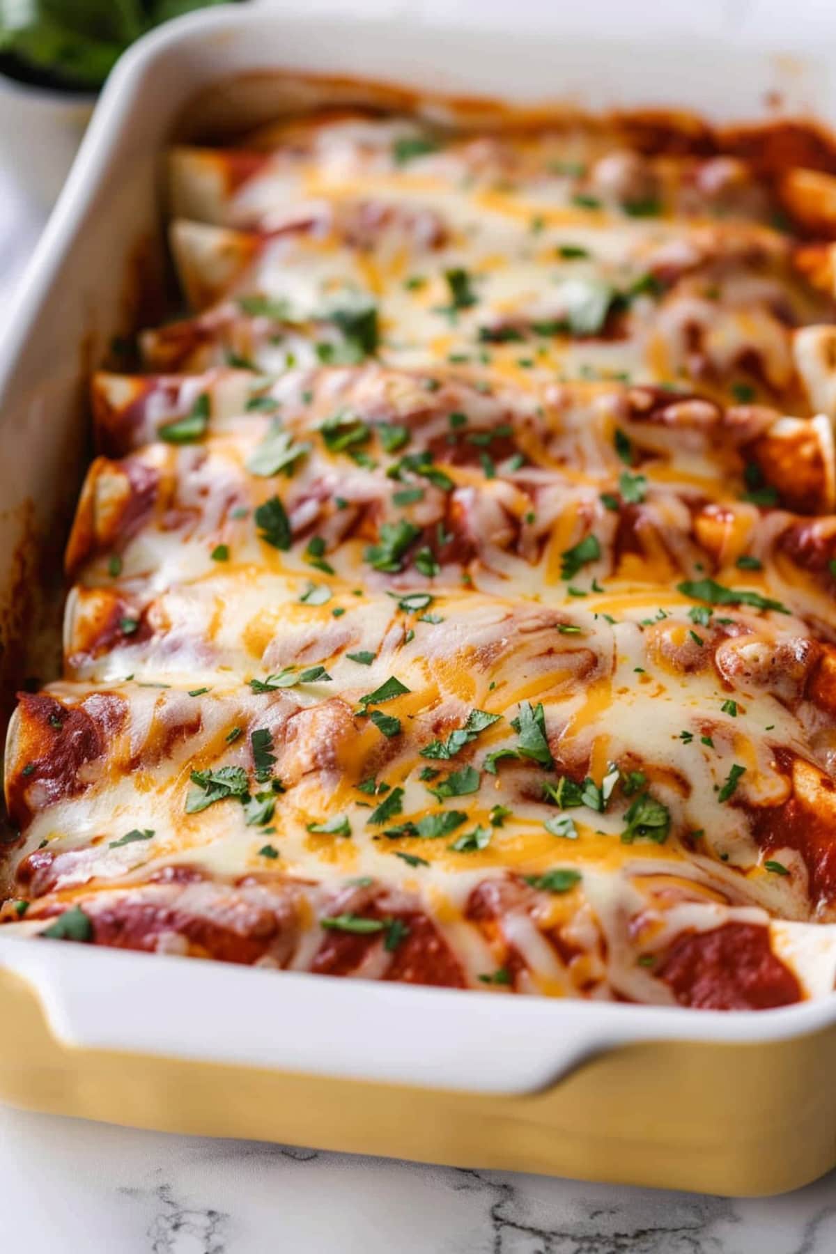 Pulled pork enchiladas on a yellow baking dish topped with melted cheese and enchilada sauce.