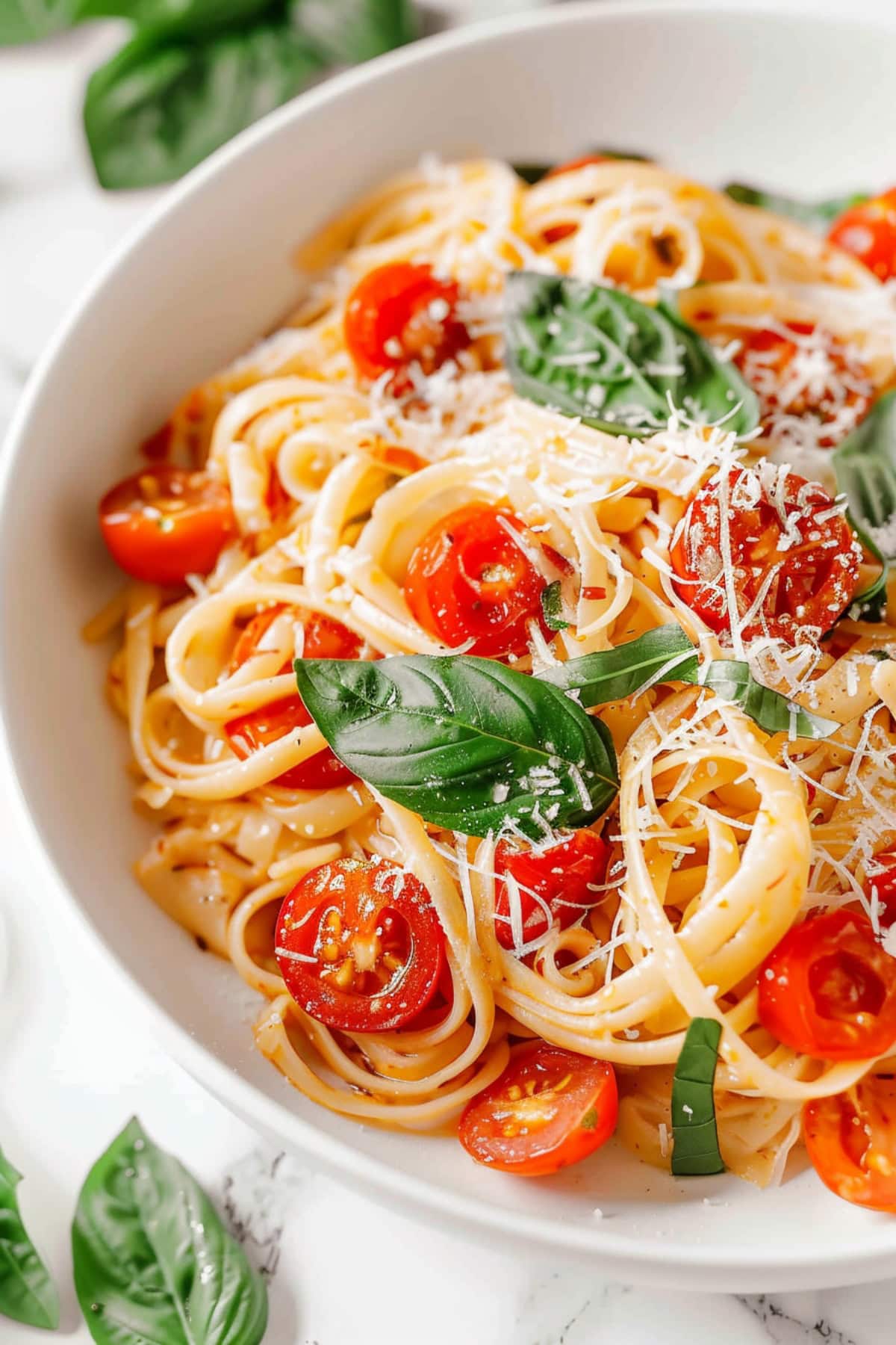 A summery pasta salad with cherry tomatoes and basil, sprinkled with black pepper and Parmesan.