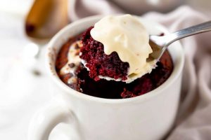 Teaspoon scooping red velvet cake with frosting in a mug.