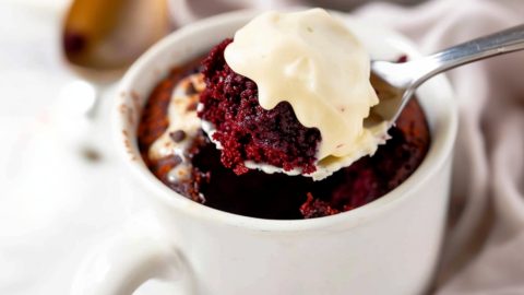 Teaspoon scooping red velvet cake with frosting in a mug.