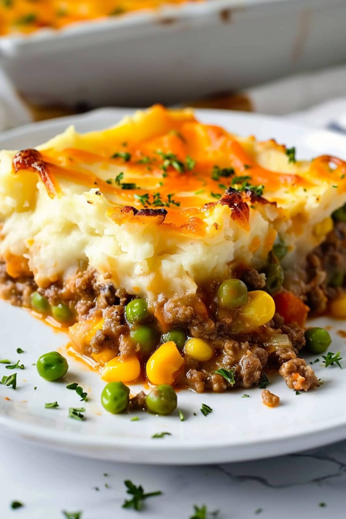 Mashed potatoes on top of ground lamb with corn kernels and green peas.