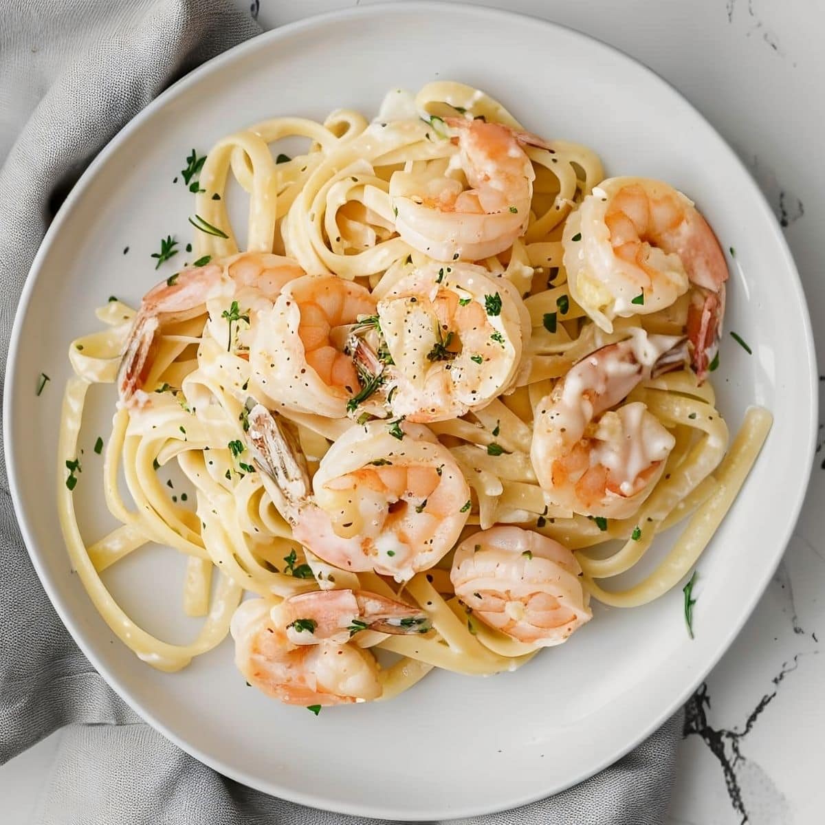 Top View of a Serving of Shrimp Alfredo on a White Plate on a White Marble Table