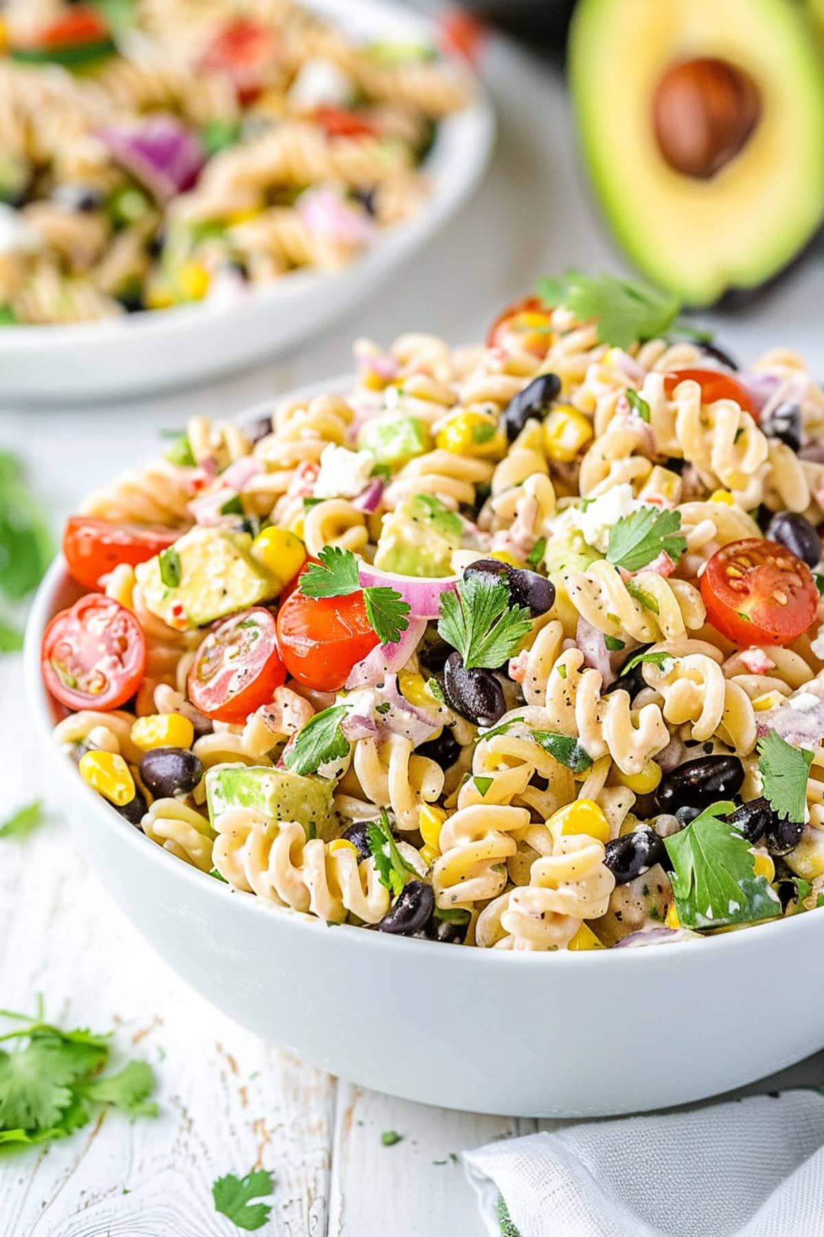 Southwest pasta salad made with rotini pasta, black beans, corn kernels, red bell pepper diced, diced red onion, cherry tomatoes, jalapeno pepper minced, fresh cilantro chopped, avocado diced, crumbled feta cheese coated in a creamy white dressing served on a white bowl.