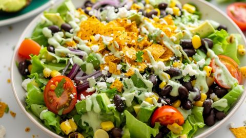 Southwestern salad made with Romaine, hearty black beans, sweet corn, crunchy veggies, salty cotija, and creamy avocado and avocado dressing garnished with chopped tortilla on top.