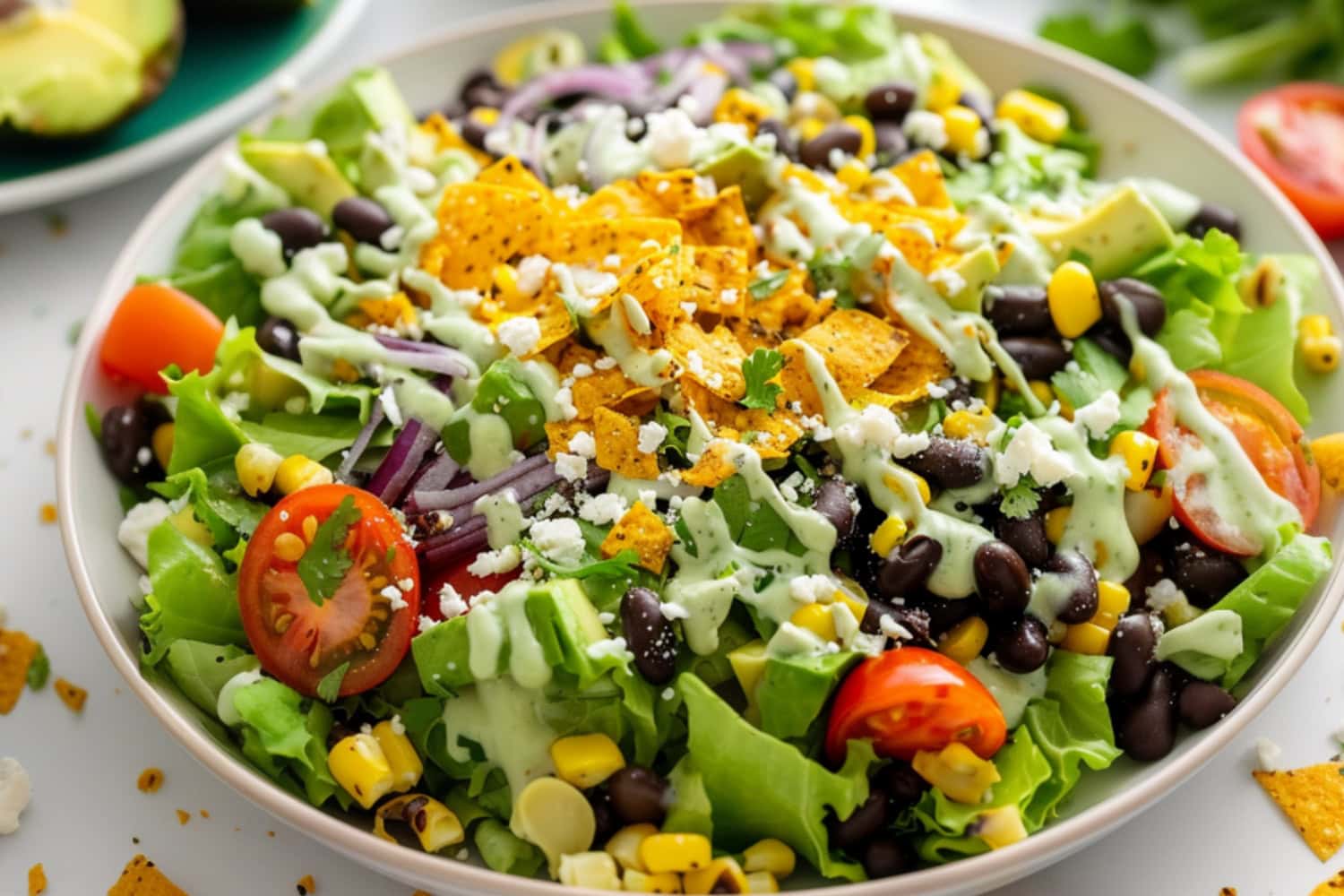 Southwestern salad made with Romaine, hearty black beans, sweet corn, crunchy veggies, salty cotija, and creamy avocado and avocado dressing garnished with chopped tortilla on top.