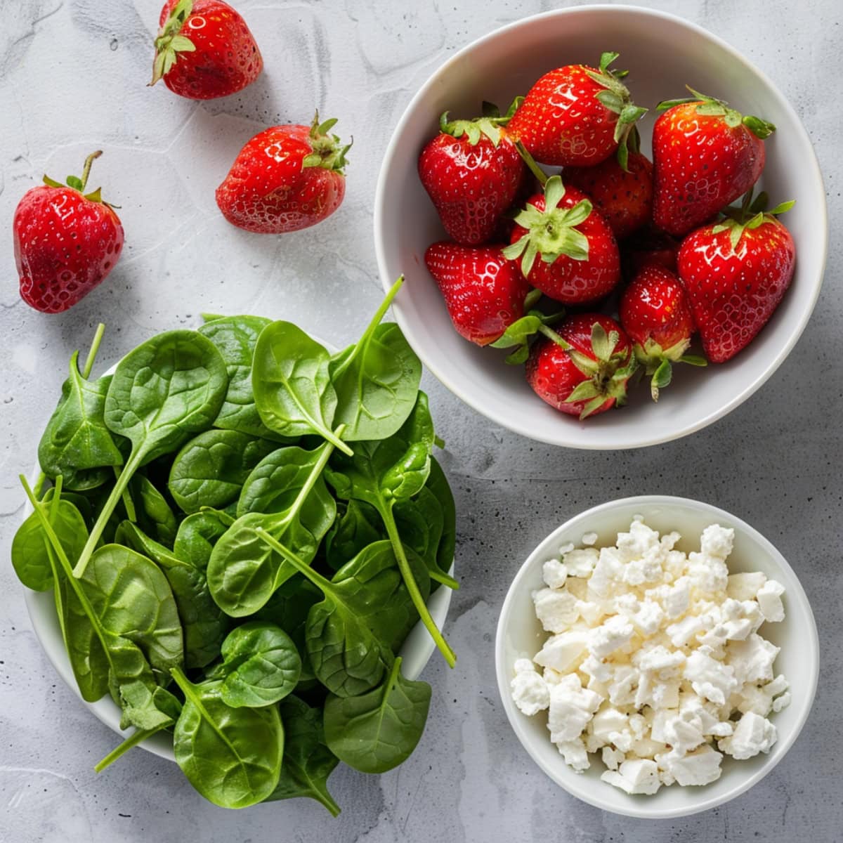 Fresh strawberries, spinach and crumbled feta cheese in a white bowl. 