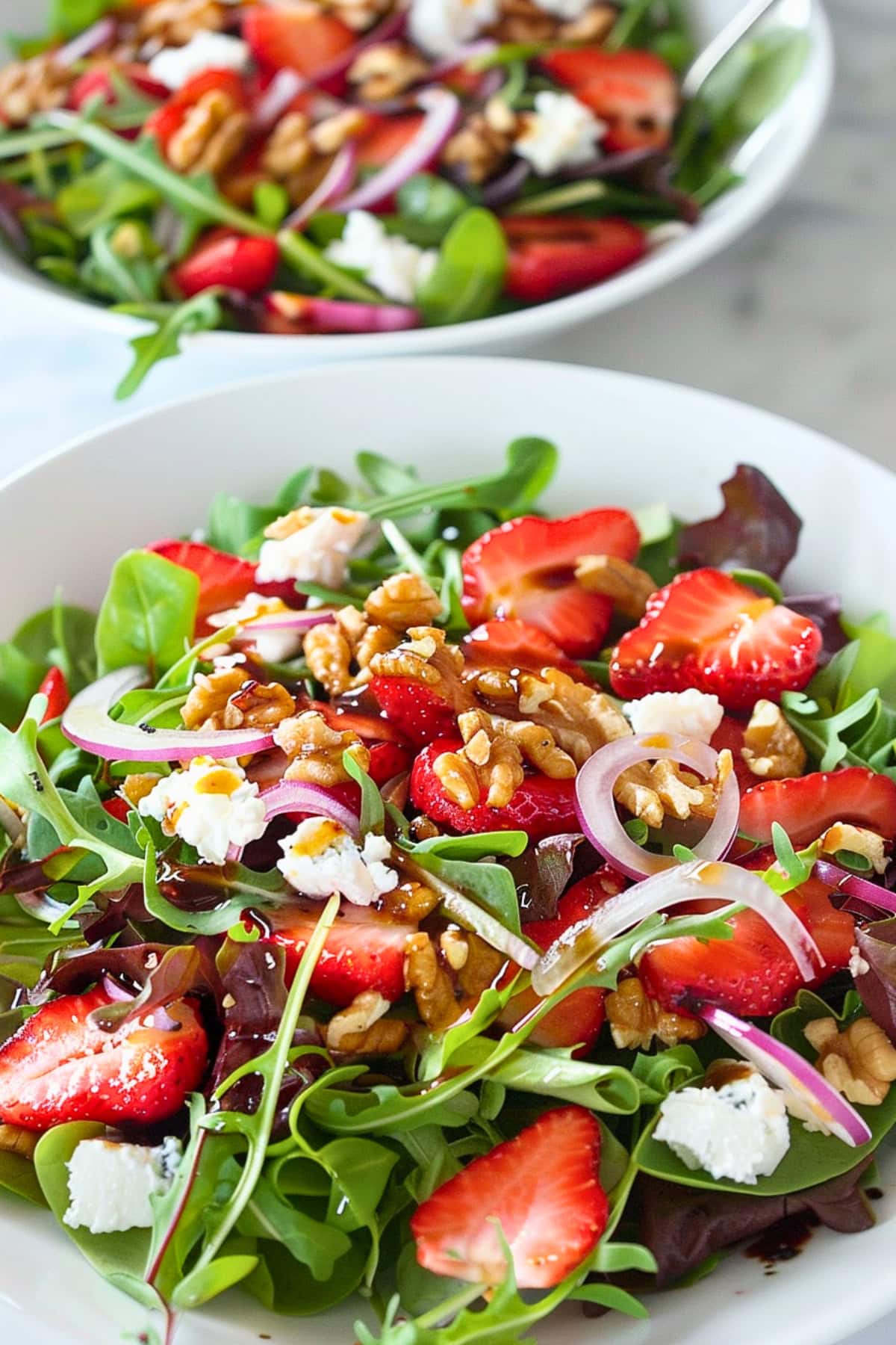 Sliced strawberries with mixed baby greens, chopped walnuts, red onions and balsamic vinaigrette served on a white plate.