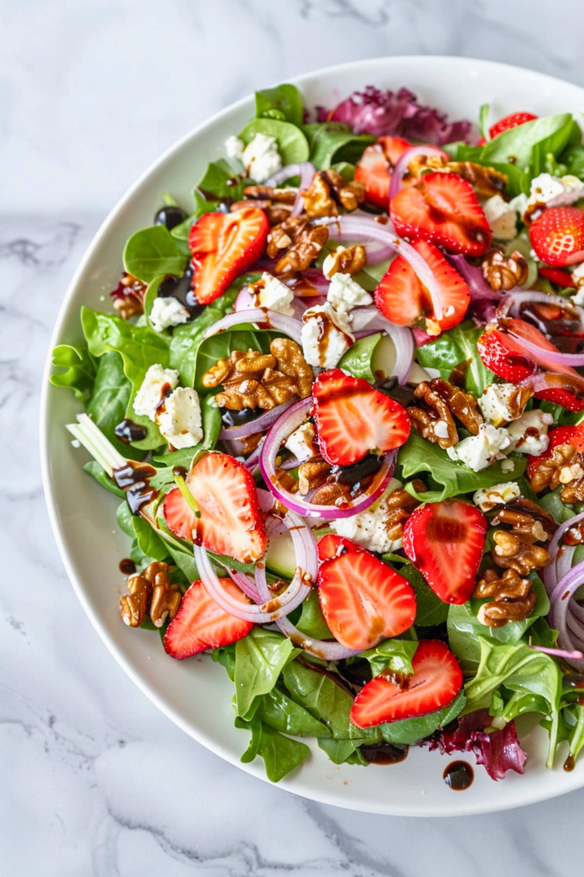Strawberry goat cheese salad made with mixed greens, sliced strawberries, red onion, and toasted walnuts served in a white plate.