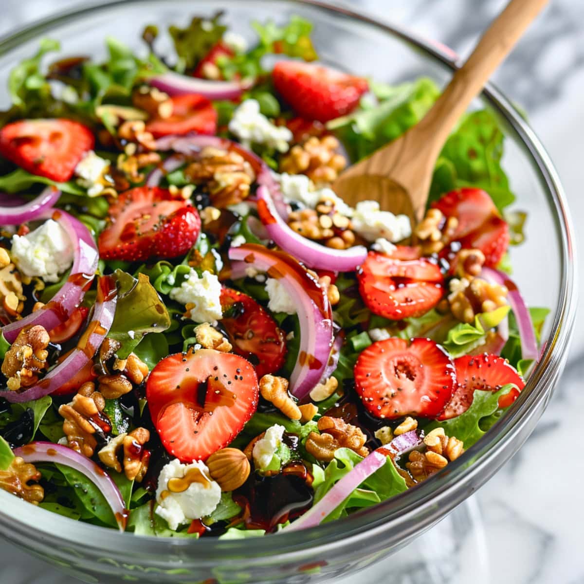 Mixed greens, sliced strawberries, red onion, and toasted walnuts tossed in a glass bowl with balsamic vinaigrette dressing.