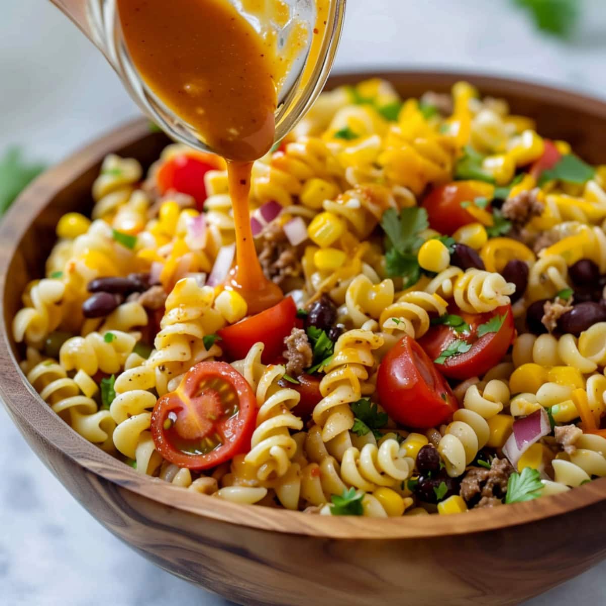 Pouring a dressing into a bowl of taco pasta salad.