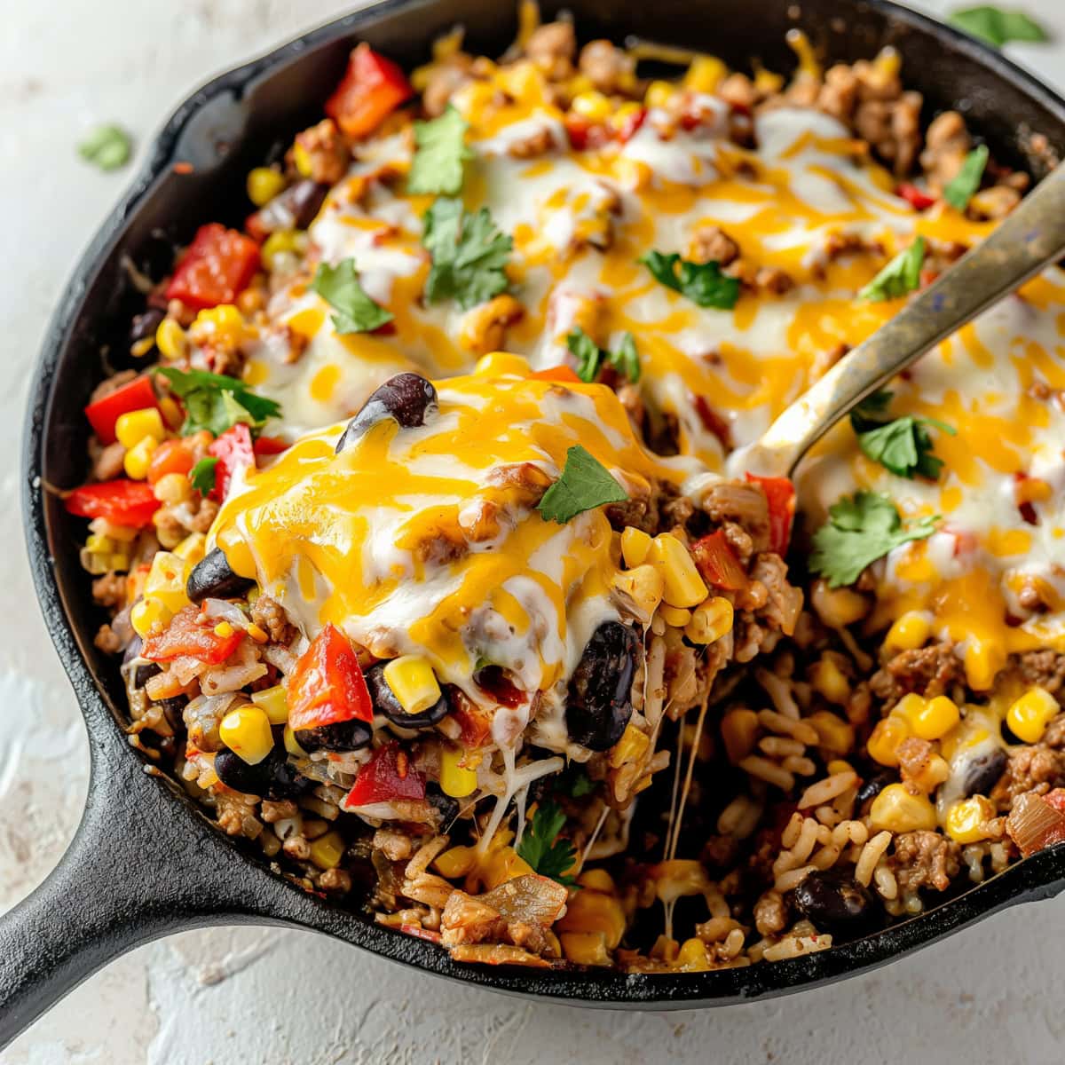 Cheesy taco skillet in a cast iron skillet made with Ground beef with diced red bell pepper, diced red onion, corn kernels, cooked rice, black beans, salsa topped with melted cheese on a cast iron skillet pan.