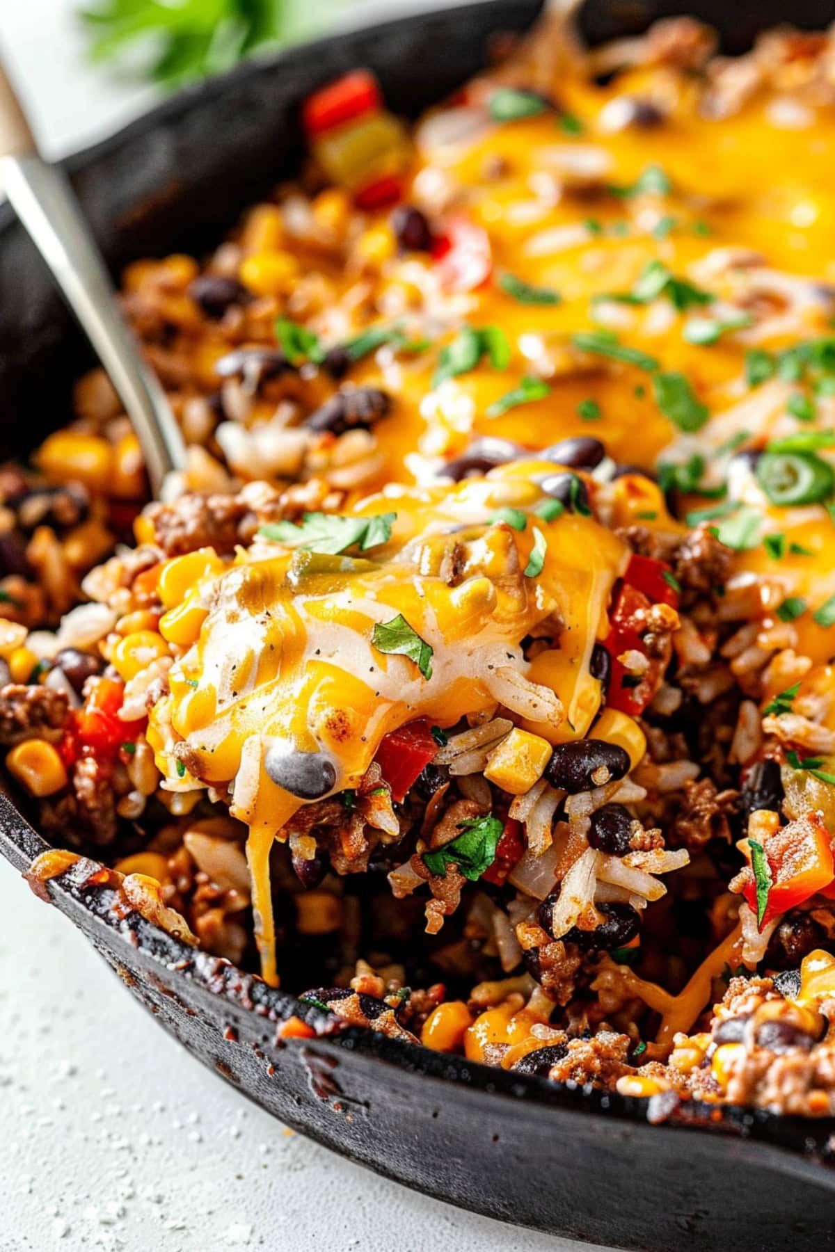 Taco made with ground beef with diced red bell pepper, diced red onion, corn kernels, cooked rice, black beans, salsa topped with melted cheese on a cast iron skillet pan