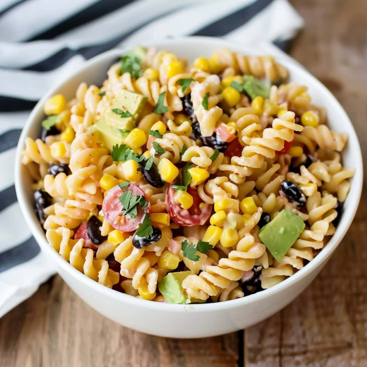 A vibrant Tex-Mex pasta salad in a white bowl, showcasing colorful ingredients like corn, black beans, cherry tomatoes, and avocado, garnished with fresh cilantro.