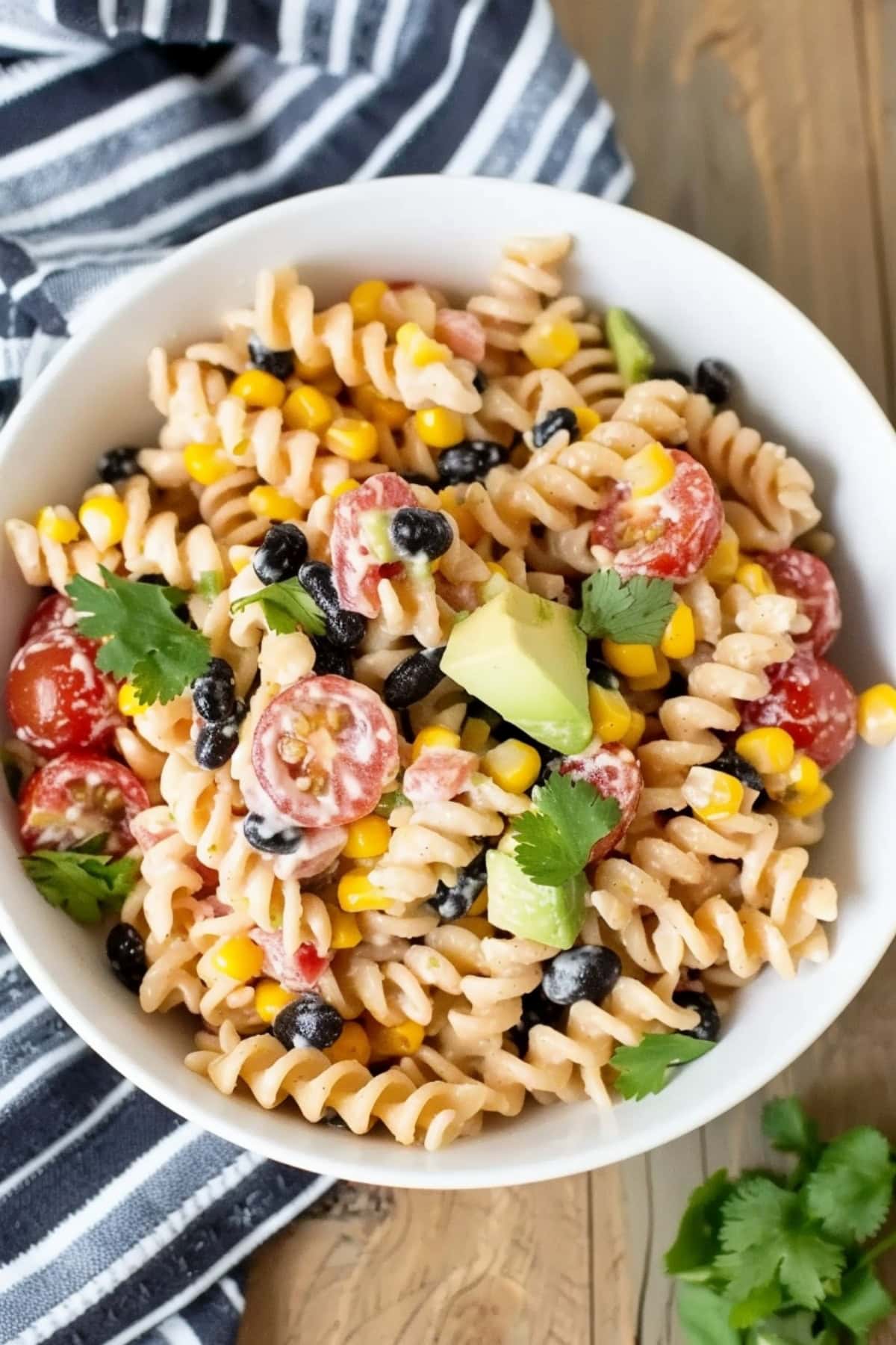 Creamy Tex Mex pasta salad with avocado chunks, cherry tomatoes, corn and black beans.