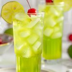 Two Glasses of Bright Green Tokyo Tea Cocktails in Tall Glasses with Ice, Cherries for Garnish, and a Lime Wheel