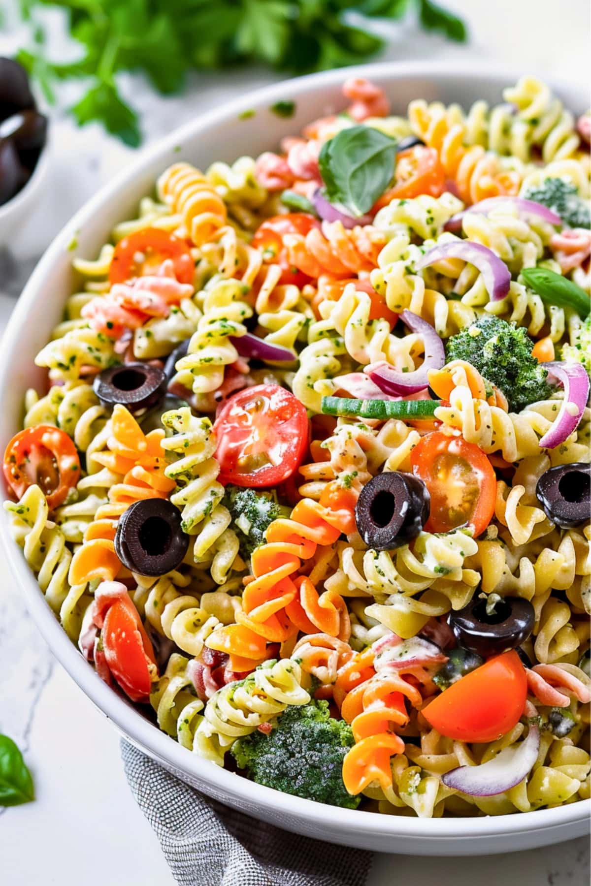 Tri color rotini pasta salad with creamy dressing with fresh herbs, pesto, veggies, and cheese served in a white bowl.