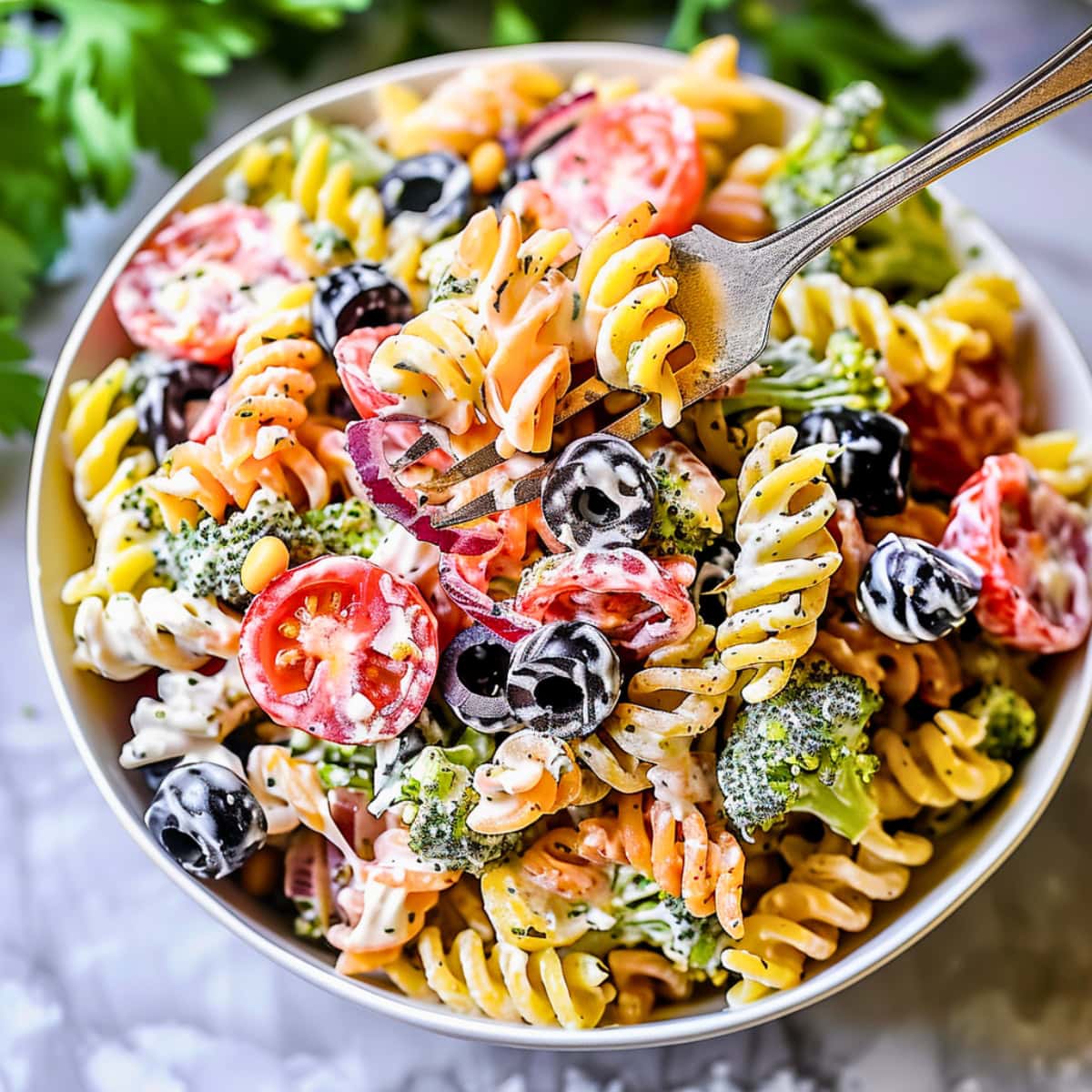Tri color pasta salad with  tri-colored rotini pasta,creamy Caesar dressing with fresh herbs, pesto, veggies, and cheese served in a white bowl. 