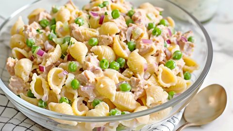 A glass bowl of creamy homemade tuna pasta salad on a white marble table.