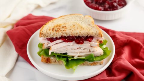 Hearty turkey cranberry sandwich with fresh green lettuce sitting in a red table cloth.