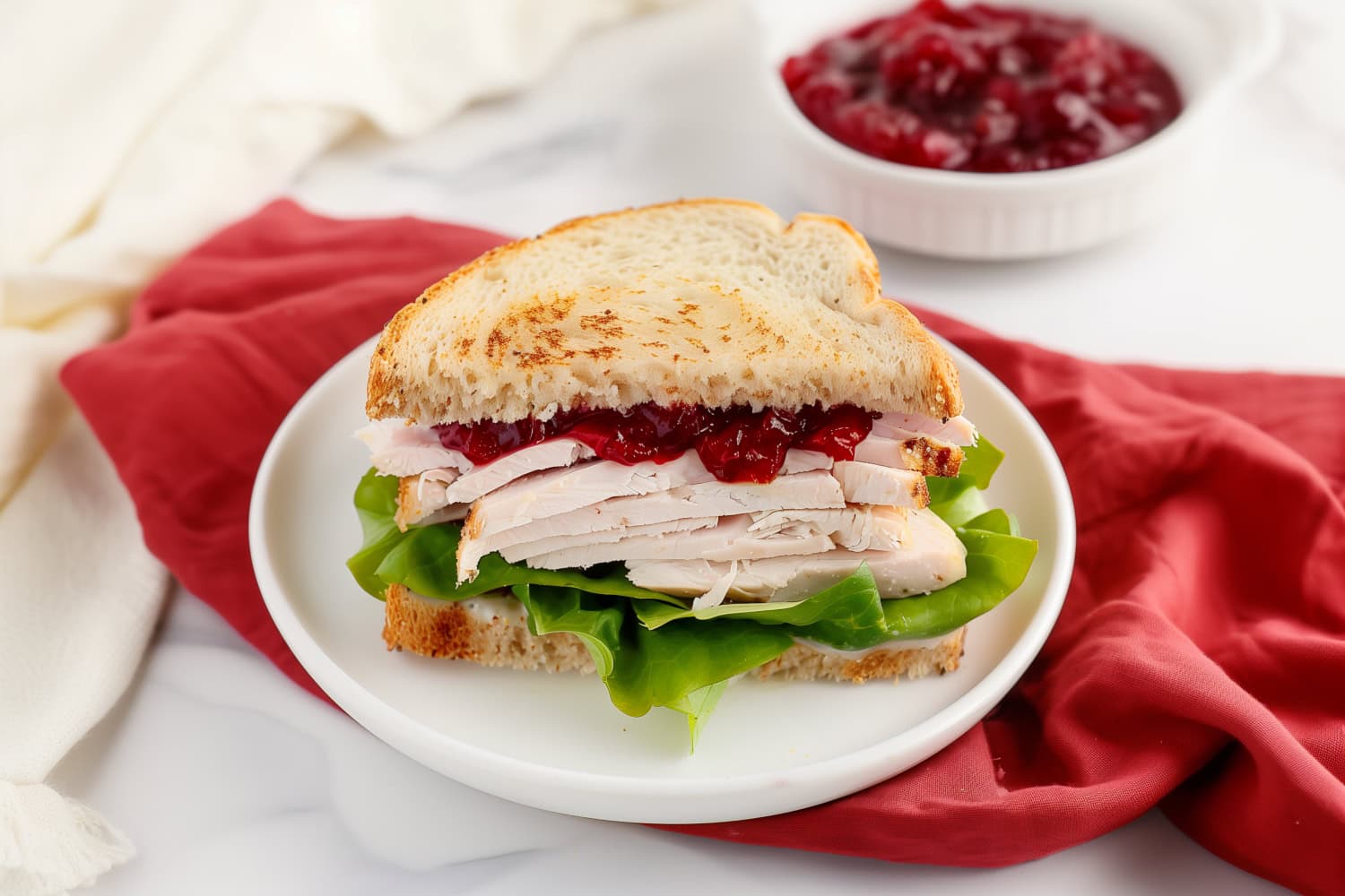 Hearty turkey cranberry sandwich with fresh green lettuce sitting in a red table cloth.