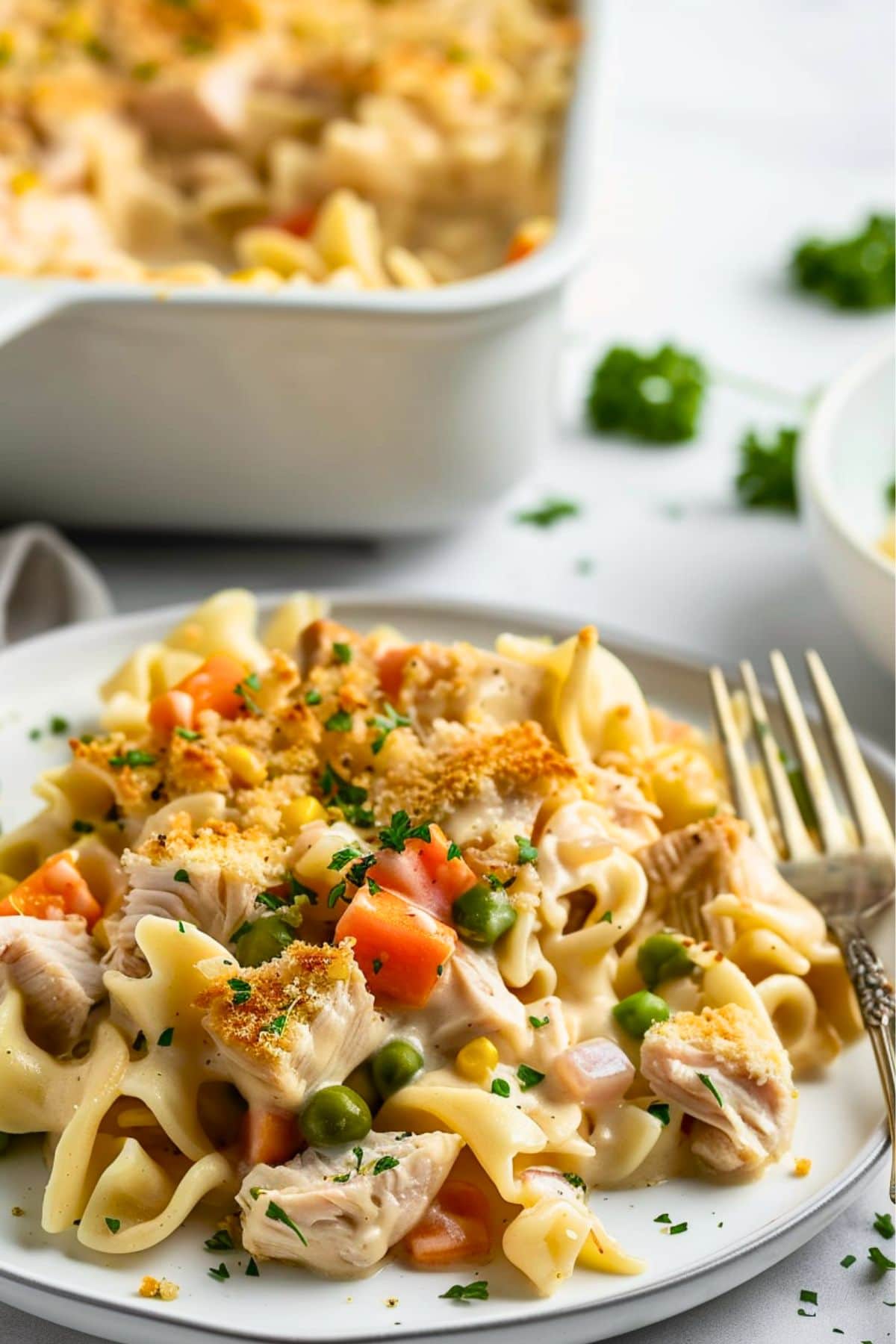 Creamy turkey noodle casserole serving on a white plate with fork.