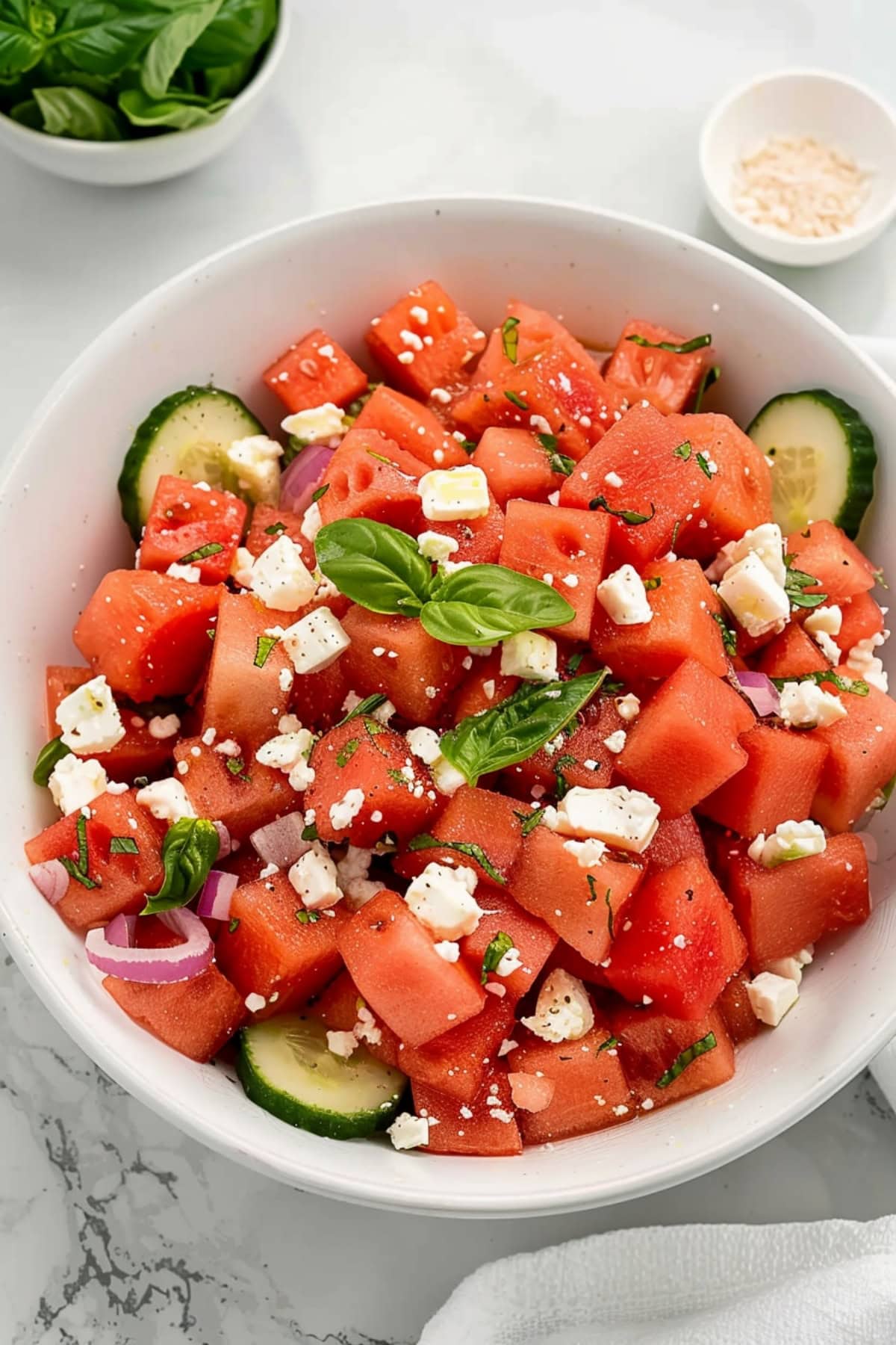 A refreshing summer salad made with sweet watermelon chunks, tangy feta cheese, and garnished with basil, served in a white bowl.