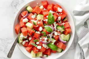 A bowl of freshly homemade watermelon salad featuring feta cheese, cucumbers and red onions.