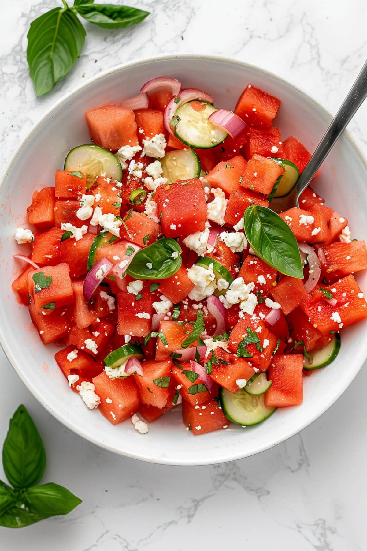 A bowl of watermelon feta salad with cucumber, red onions and basil.
