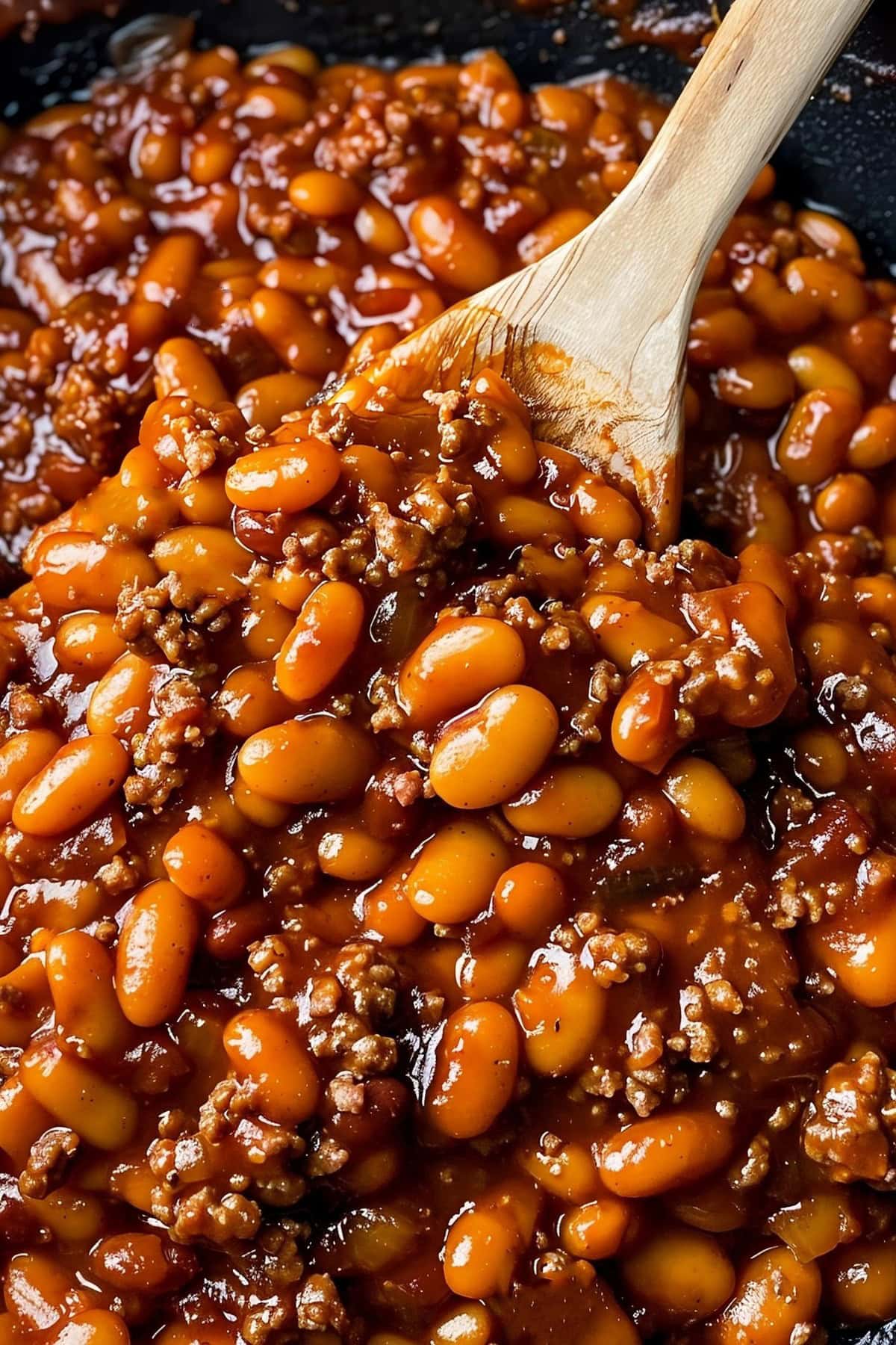 Close Up of BBQ Baked Beans with Beans, Ground Beef, and Sauce in a Cast Iron Skillet with a Wooden Spoon