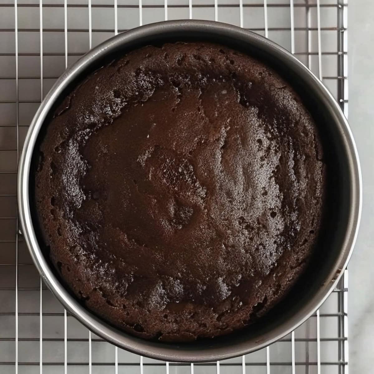 Unfrosted Chocolate Truffle Cake in a moulder on top of a cooling rack.