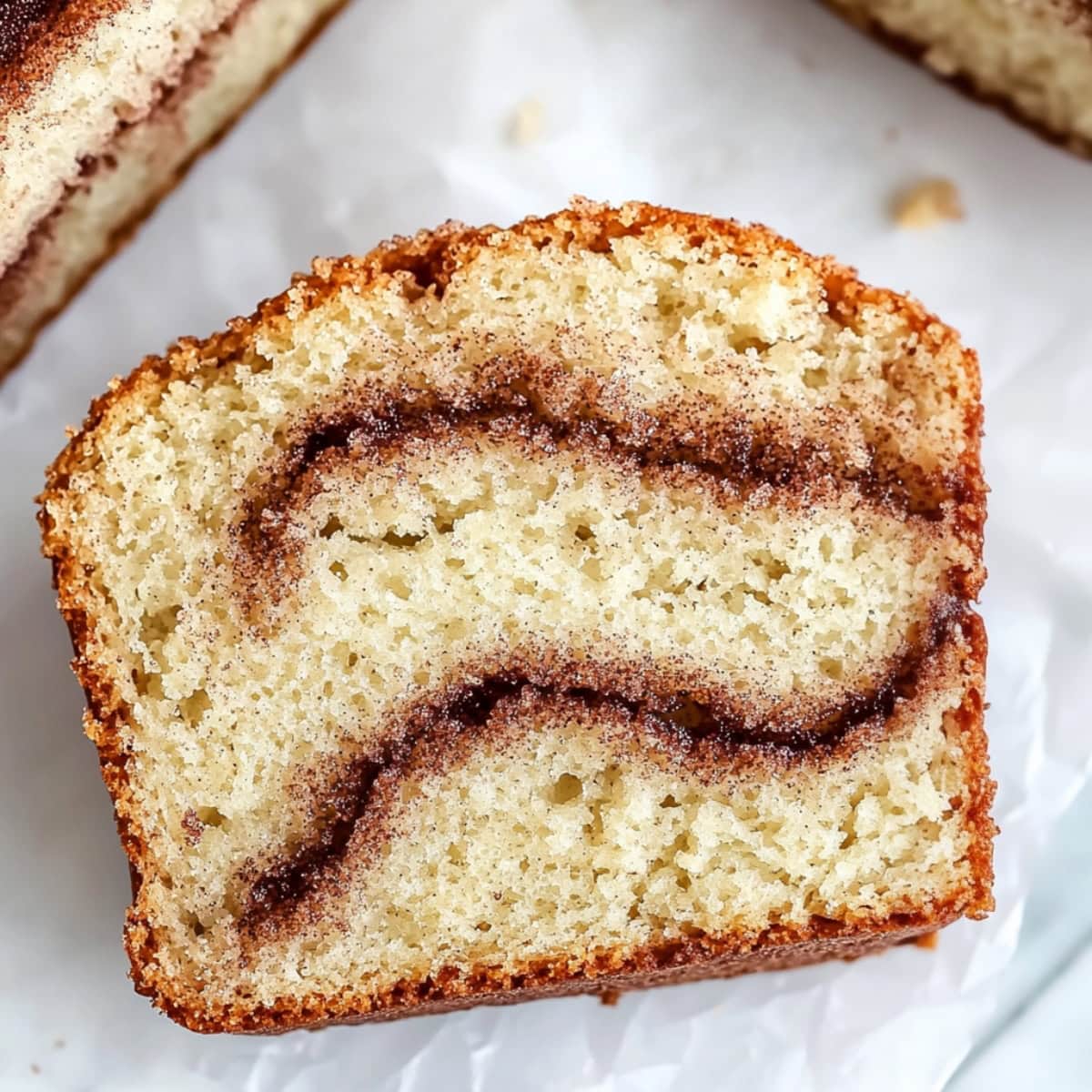 A piece of sliced cinnamon swirl quickbread on a parchment paper.